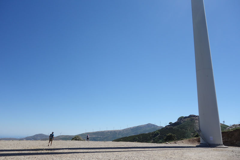 persons walking under gigantic wind-turbine